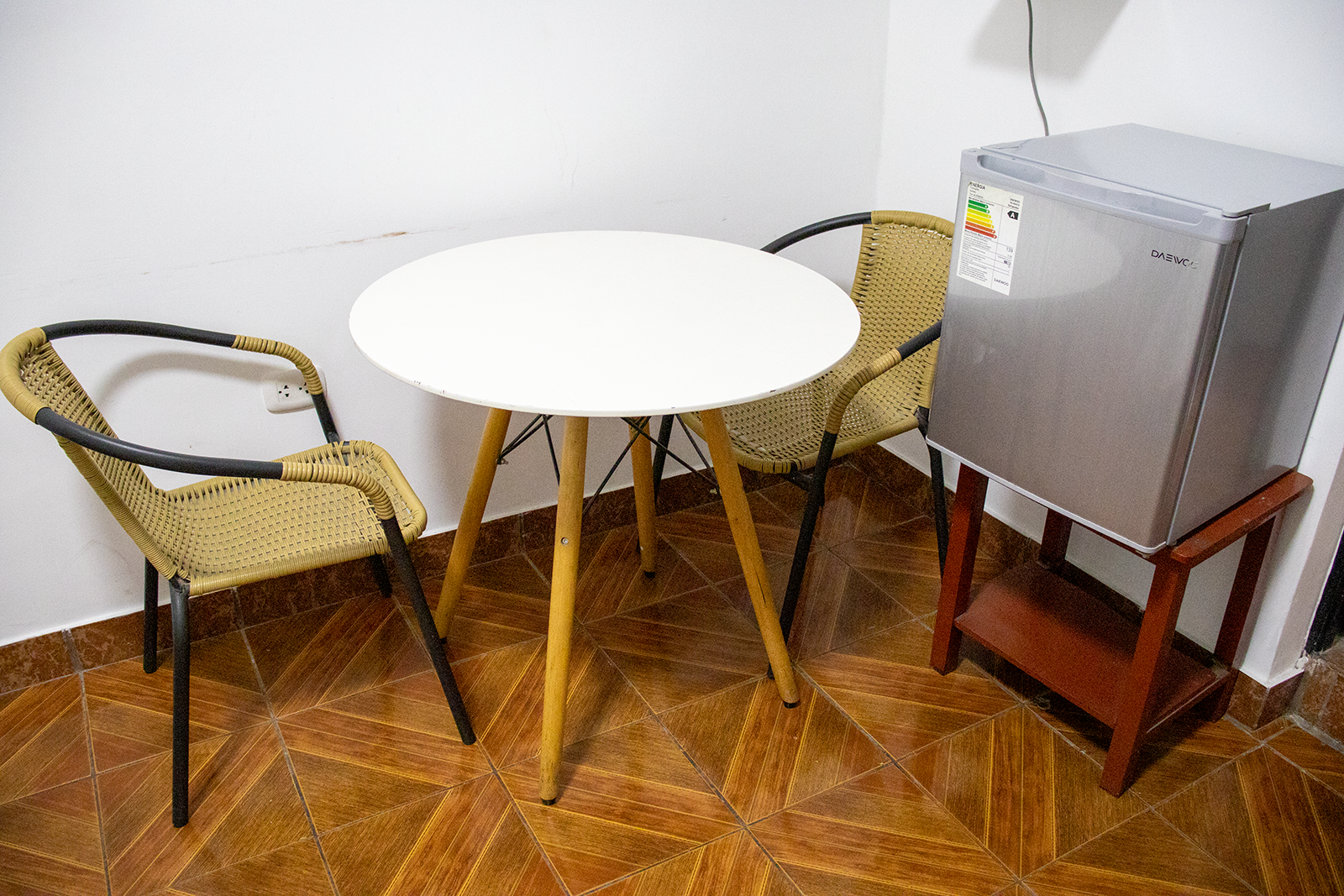 A small white table, two chairs, and a mini-fridge in a corner of a room.