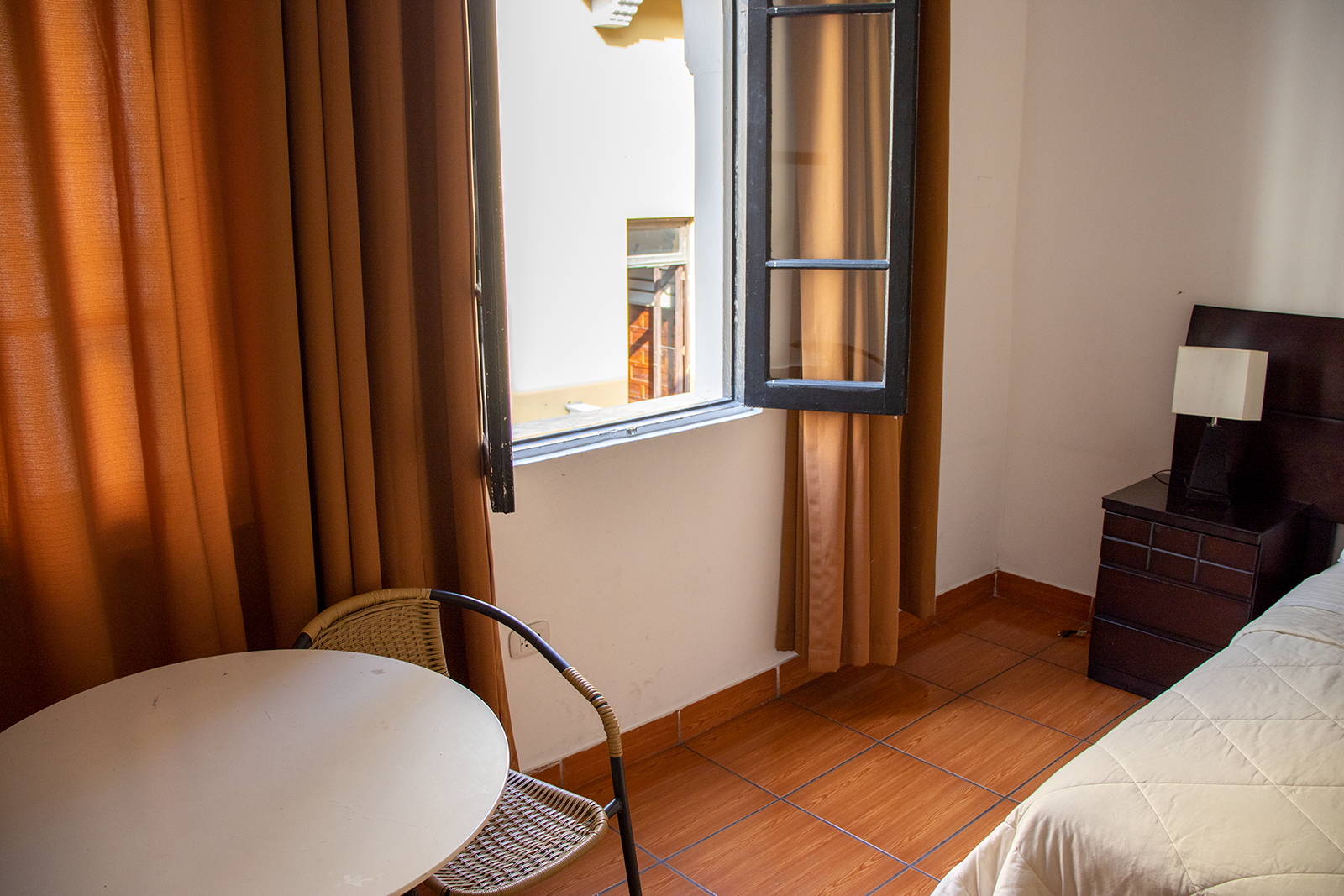 Room with bed, nightstand, and chairs with an open window letting in sunlight.