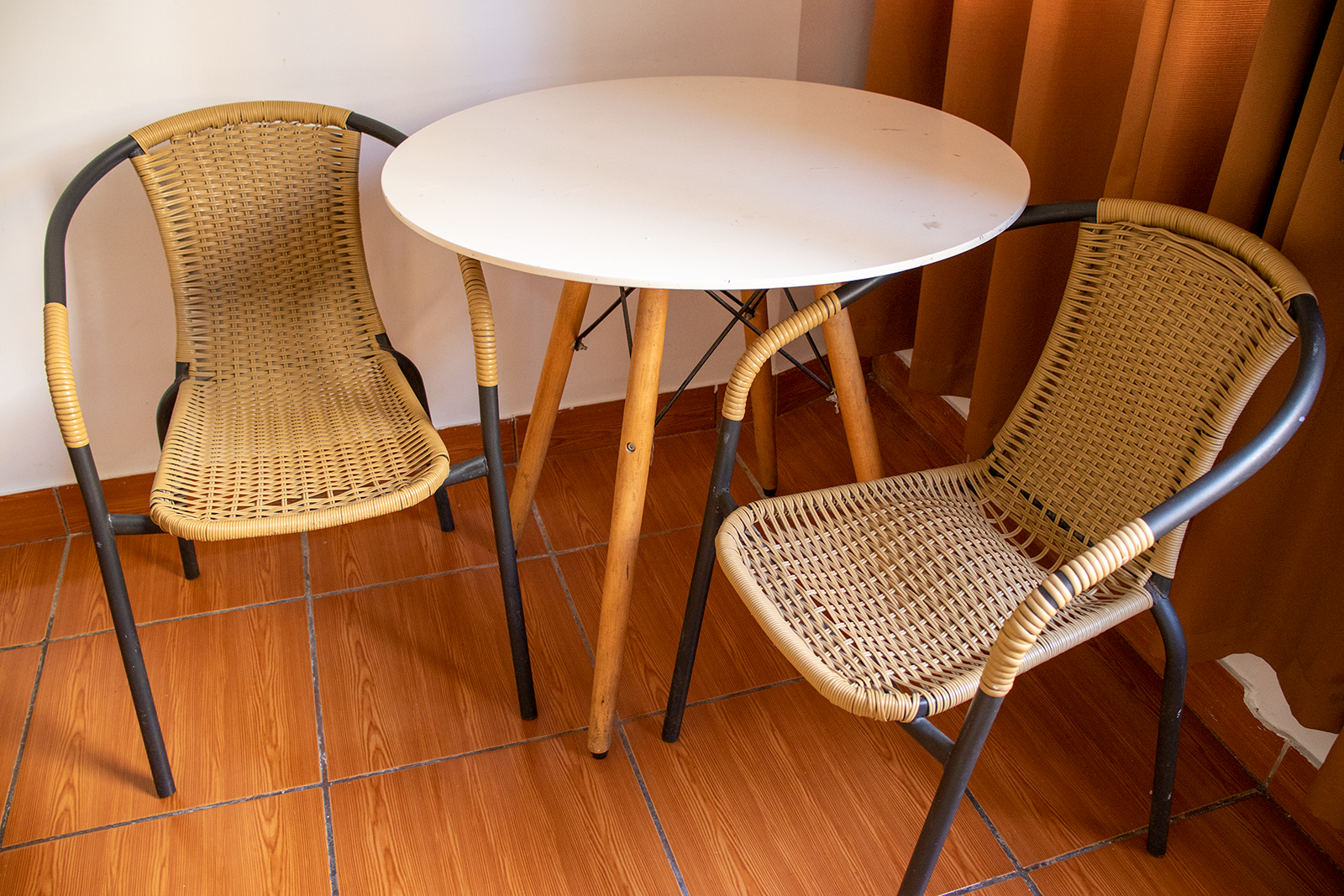 Small white table with two woven chairs in a room with wooden floor and curtains.
