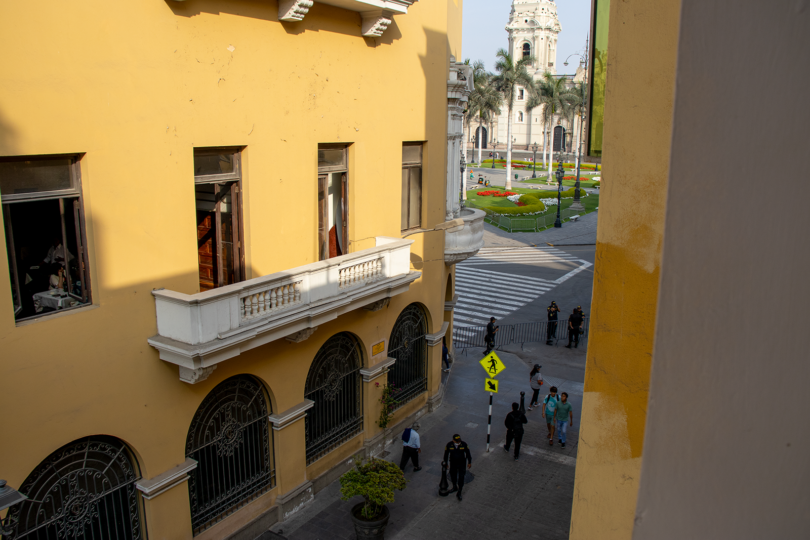 Yellow building overlooking a plaza with people, church in background.