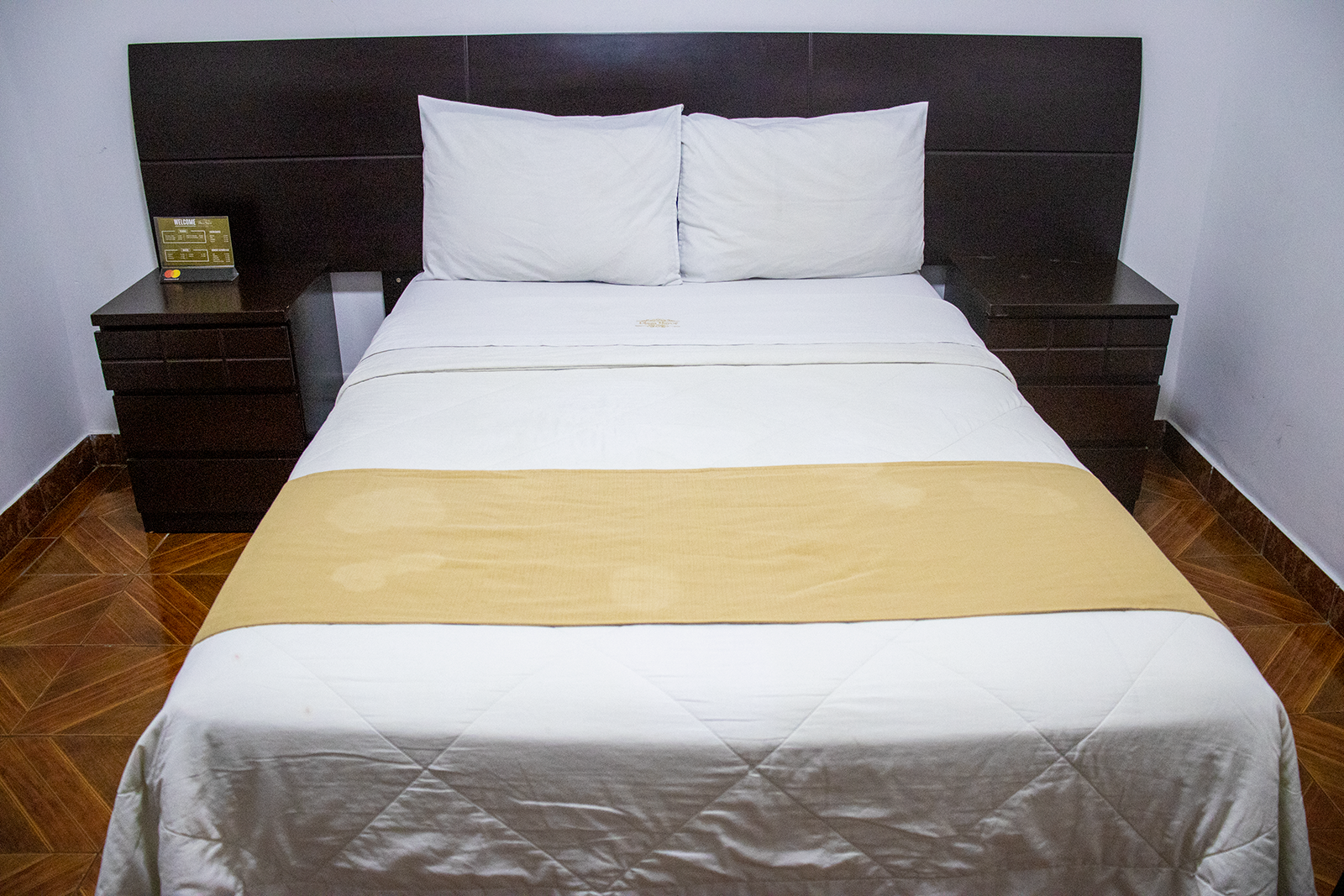 Bedroom with a bed, two nightstands, white bedding, a gold bed runner, and a dark brown headboard.