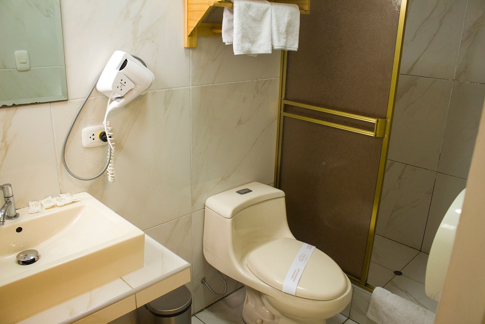 Bathroom with sink, toilet, shower, and hairdryer. White and cream tones with gold trim.