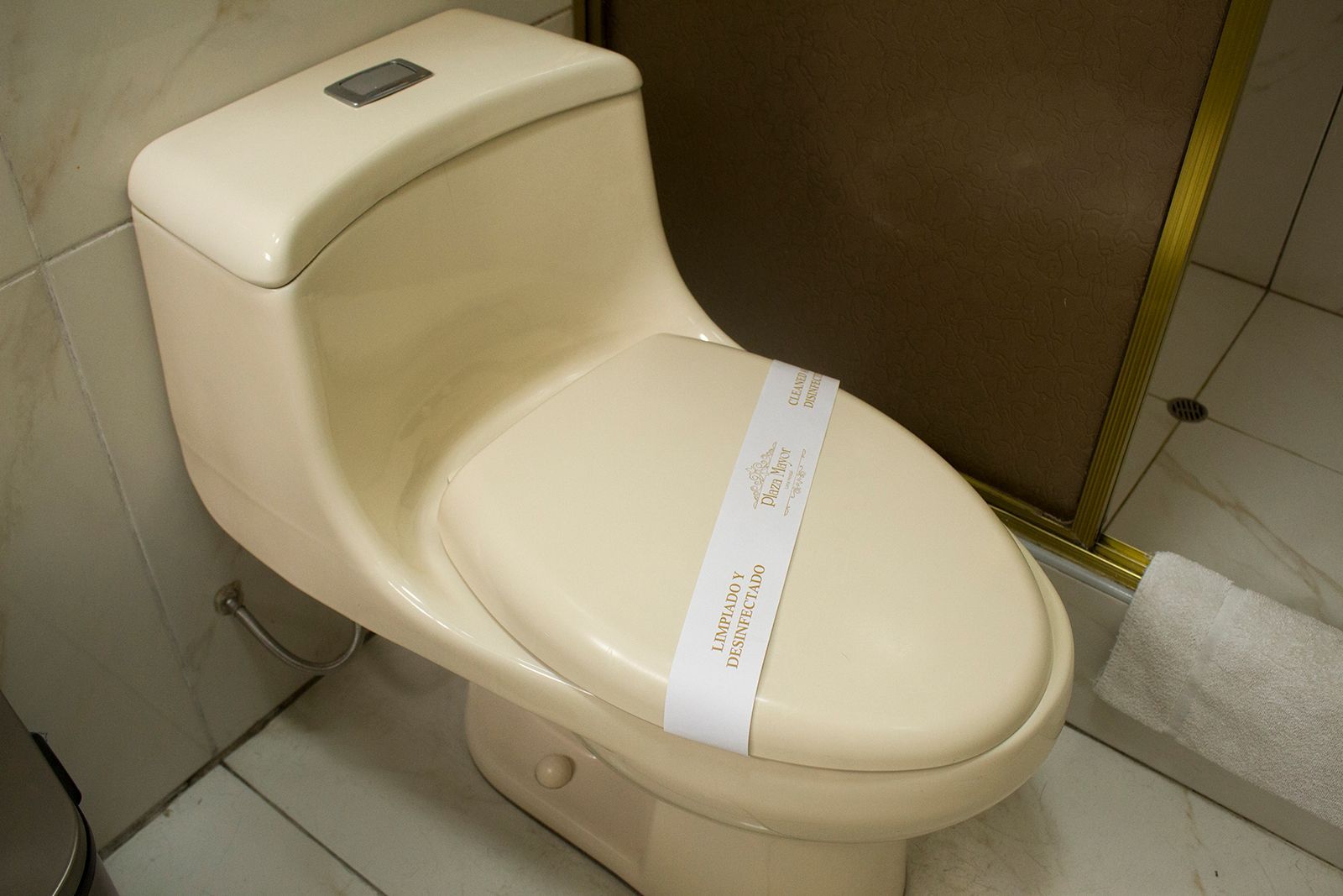 Cream-colored toilet in a bathroom; the seat has a paper strip across it.