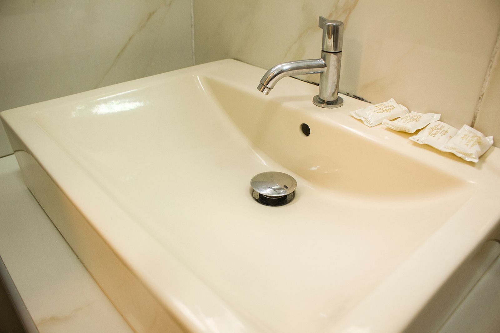 Off-white bathroom sink with a chrome faucet and drain stopper. Two folded white cloths rest on the rim.