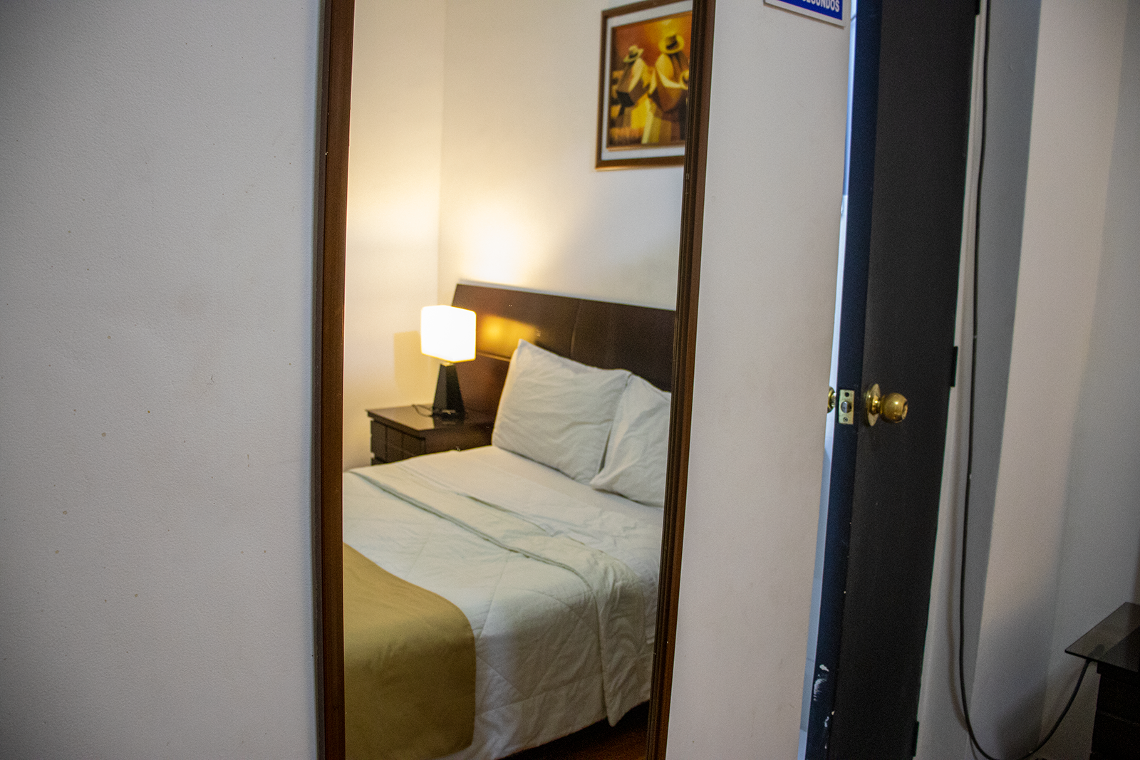 Mirror reflecting a hotel room with a bed, nightstand, and artwork.