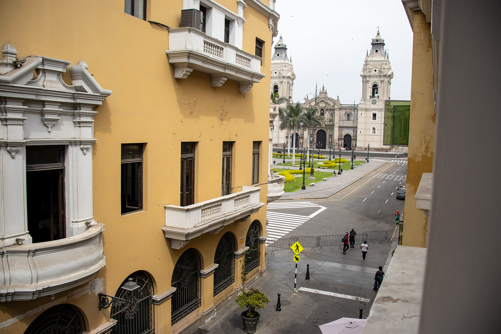 Yellow building with balconies overlooking a street and a cathedral in Lima, Peru.