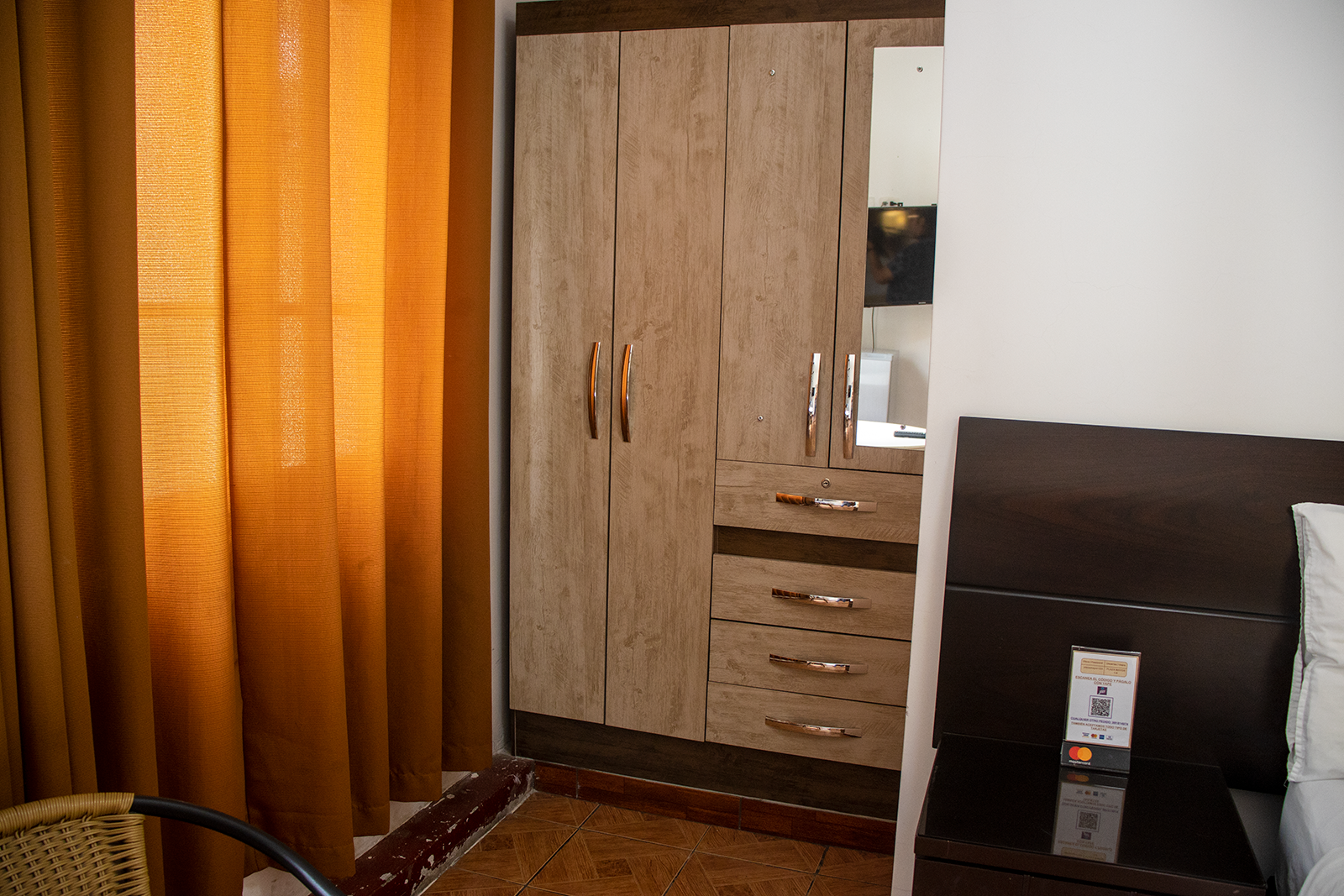 Closet and nightstand in a hotel room. Beige closet with mirror, drawers, and gold handles, next to a dark nightstand.