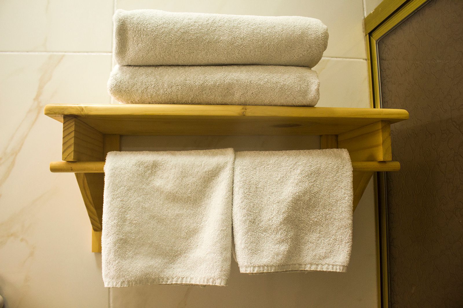White towels stacked and hanging on a wooden shelf against a tiled wall.