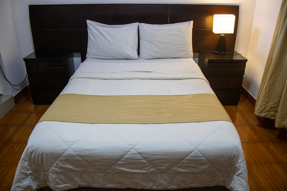 Una cama en una habitación de hotel con dos almohadas, un camino de cama de color tostado y dos mesitas de noche.