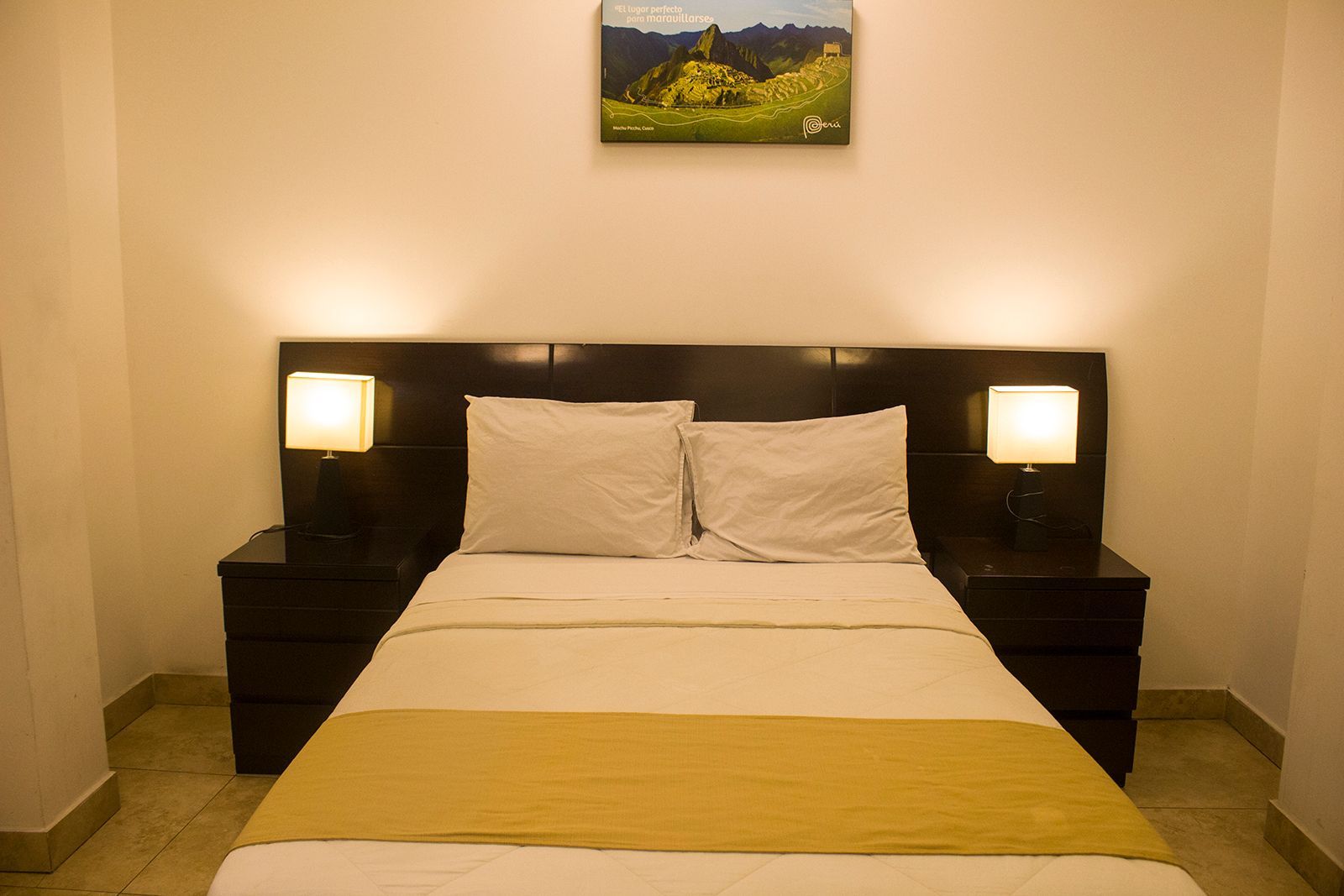 Bedroom with a made bed, bedside tables with lamps, and a landscape picture on the wall.