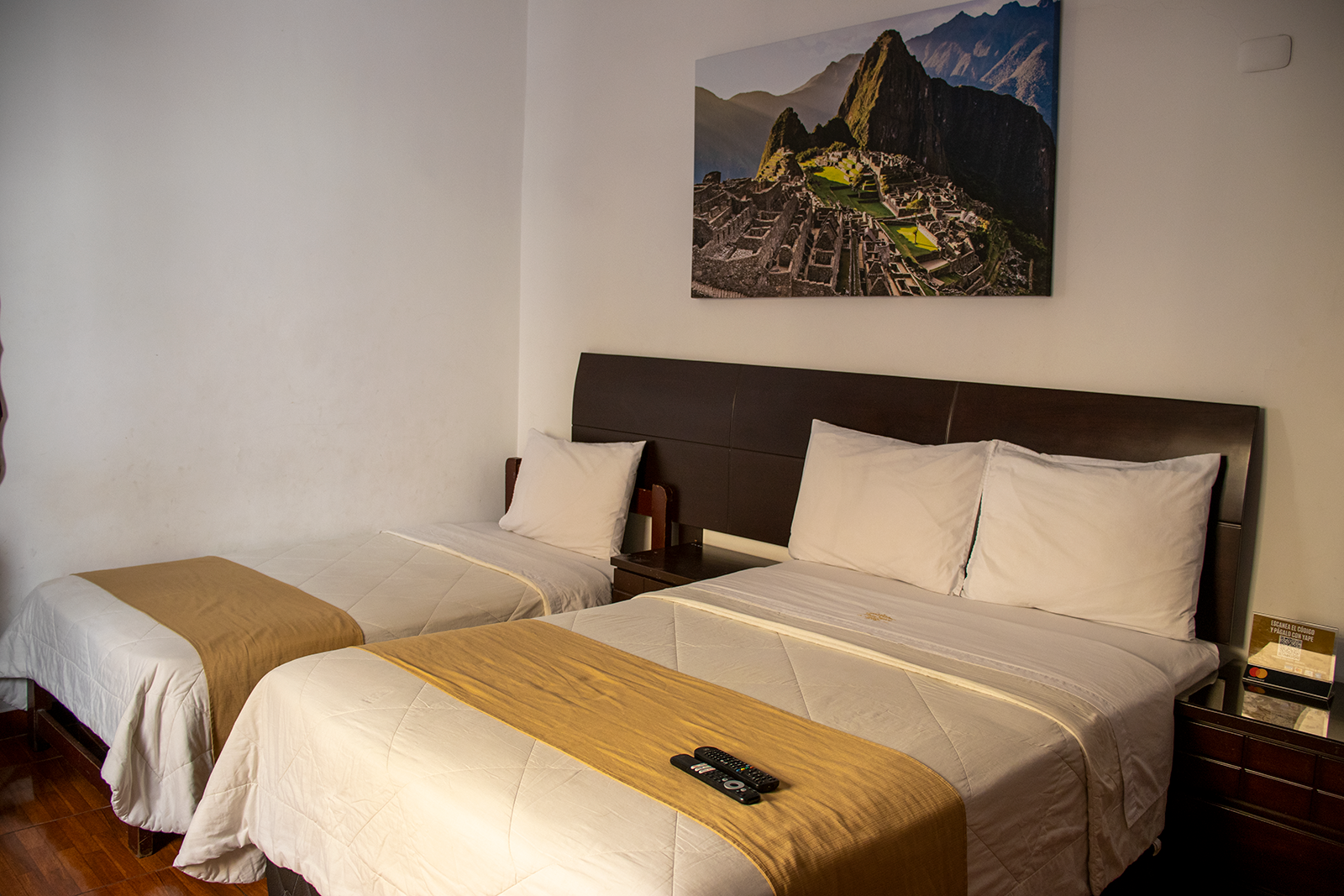 Dormitorio con dos camas, una matrimonial y una individual, y una lámina de Machu Picchu en la pared.