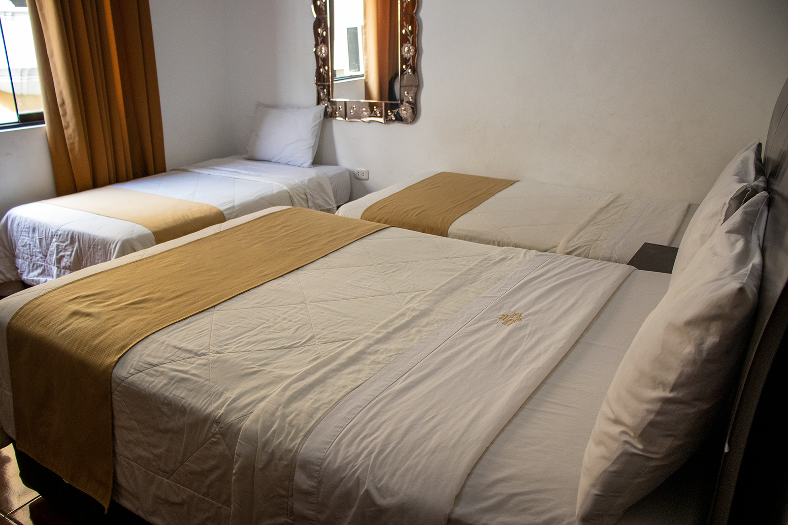 Una habitación de hotel con una cama doble y una cama individual, ropa de cama blanca y detalles dorados.