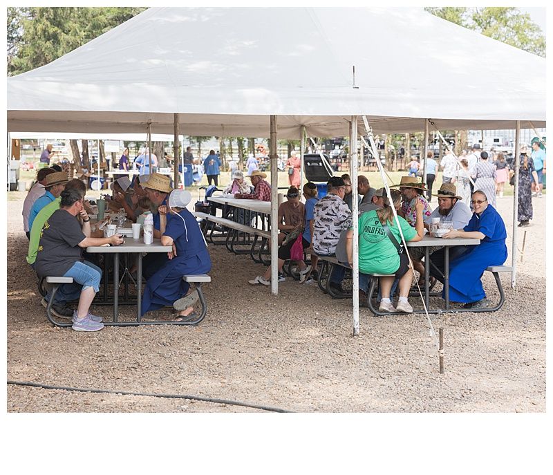 People seated at picnic tables under a large white tent at an outdoor gathering