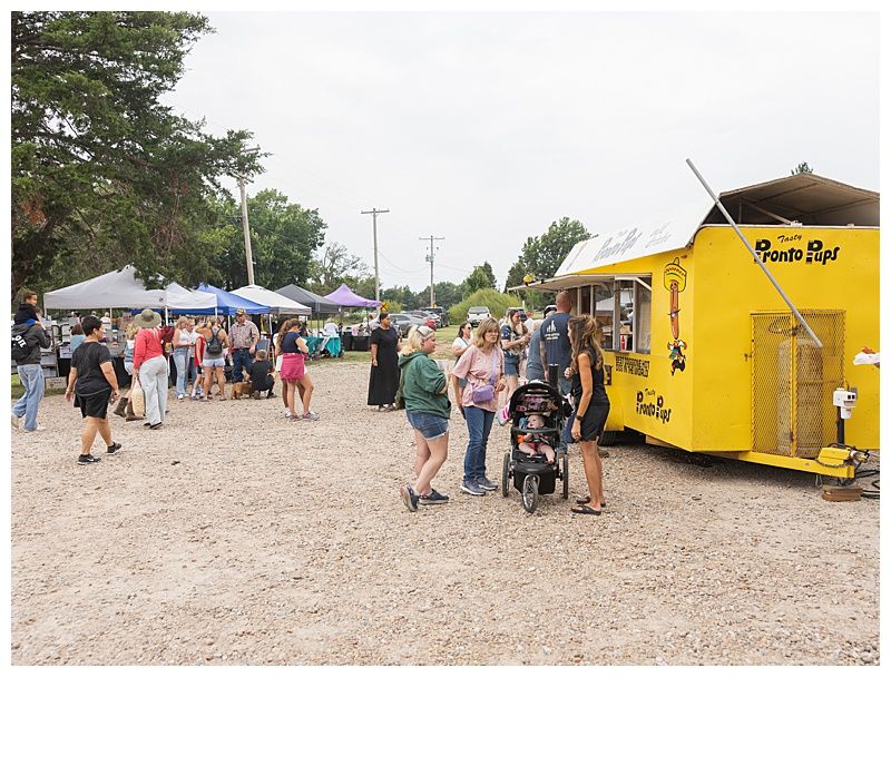 Outdoor market with white tents and people gathered beside a bright yellow food truck.