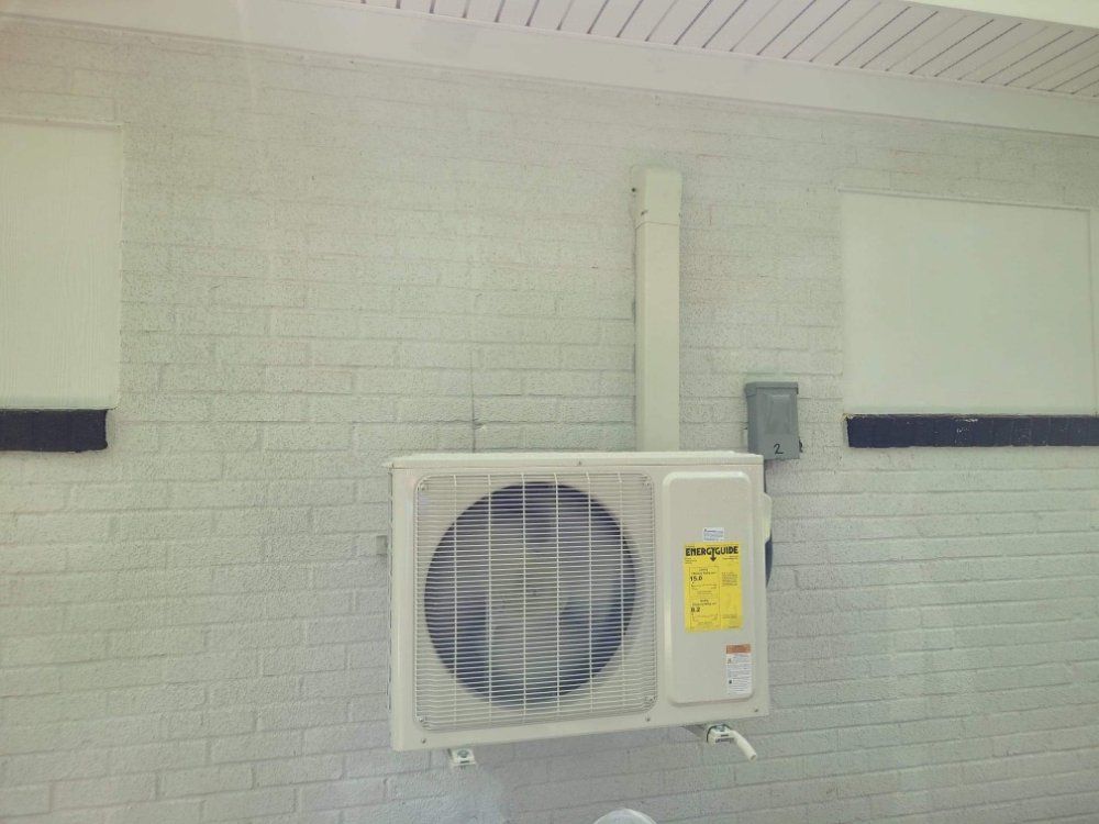 Wall-mounted outdoor air conditioner unit on a white brick wall beneath a ceiling overhang.