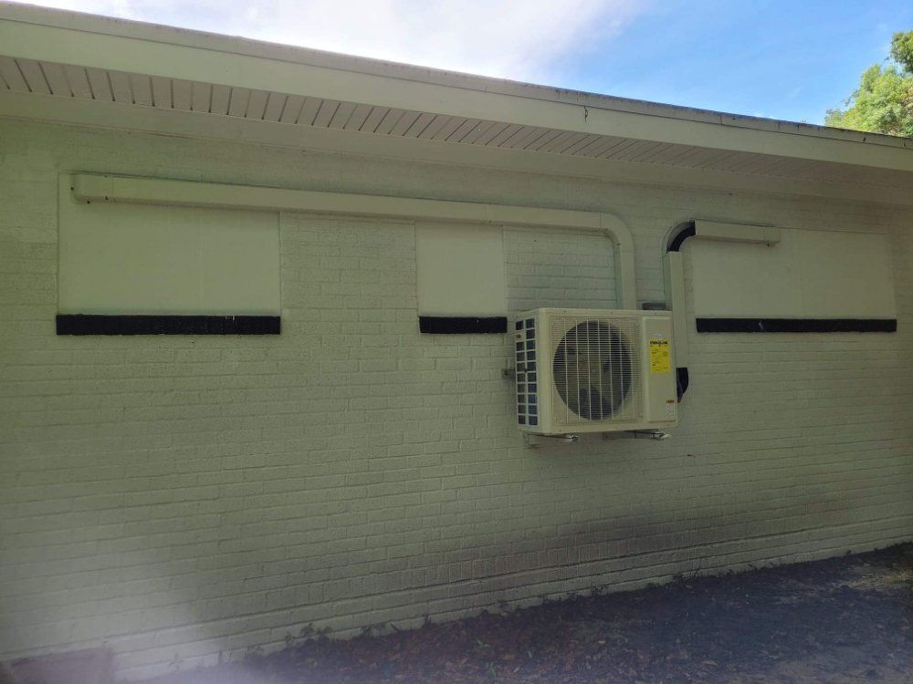 White brick exterior wall with two windows and a mounted air conditioner unit