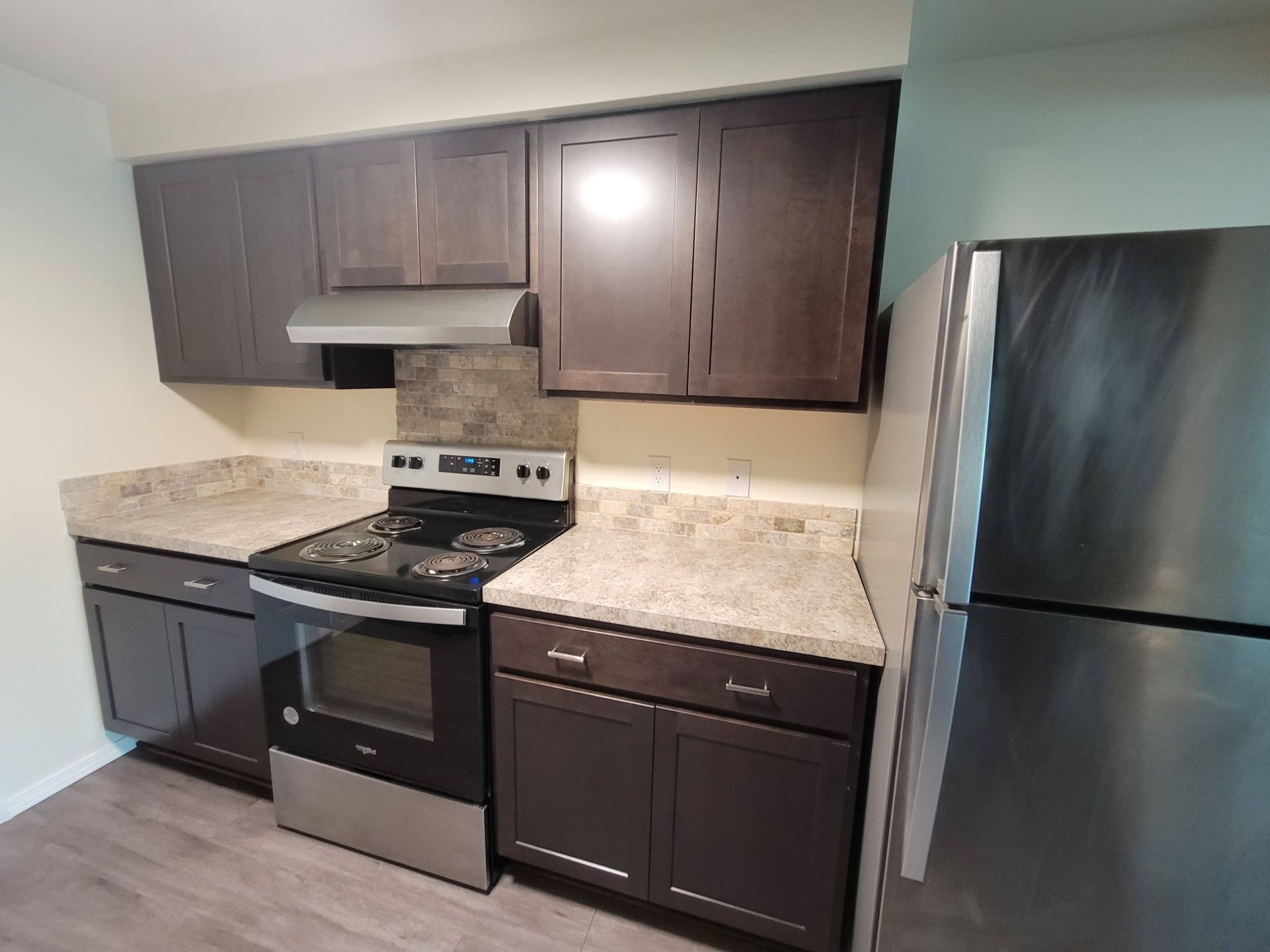 A kitchen featuring dark wood cabinets, a stainless steel stove and refrigerator, and light speckled countertops.
