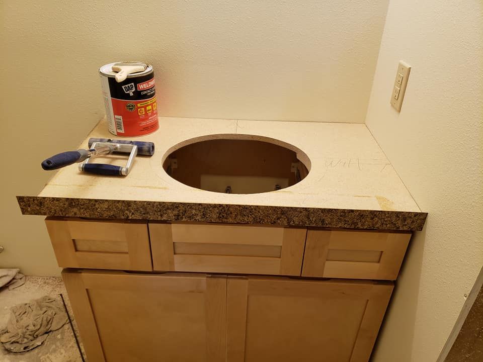 A bathroom vanity with a partially installed countertop, a can of contact cement, and a roller tool on top.