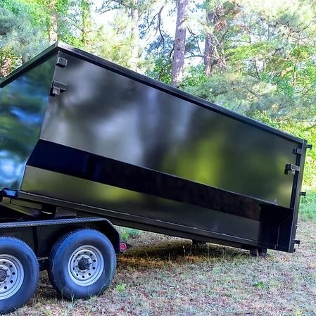 Black dump trailer tipped on a wooded slope, hitched to a dual-axle truck