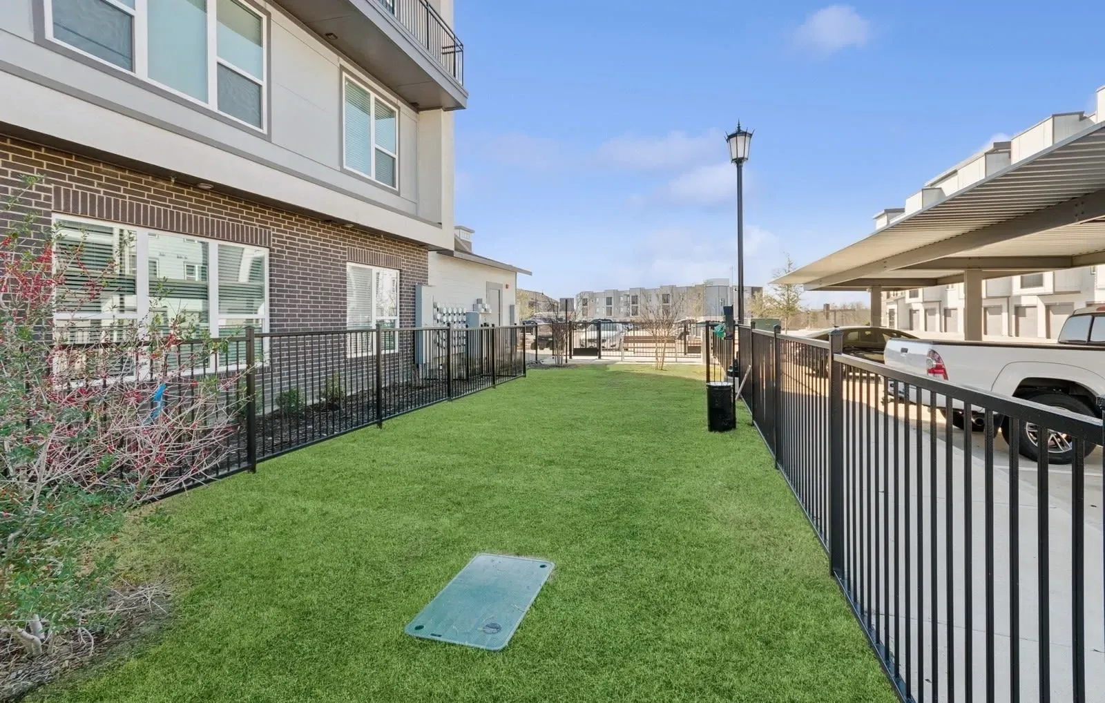 Grassy communal courtyard with a black metal fence, adjacent apartment building, and a streetlamp. Experience comfort in our thoughtfully designed three-bedroom apartments in Rowlett, TX—schedule your visit today.