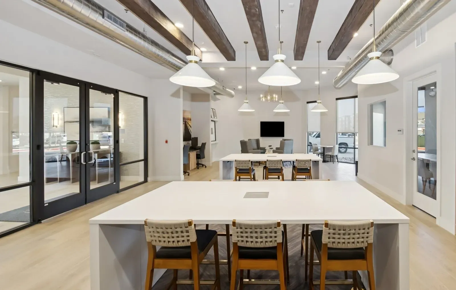 Interior communal lounge with long white tables, pendant lights, glass doors, and exposed ductwork. Tour our inviting one-bedroom apartments in Rowlett, TX and discover a space that works for you.