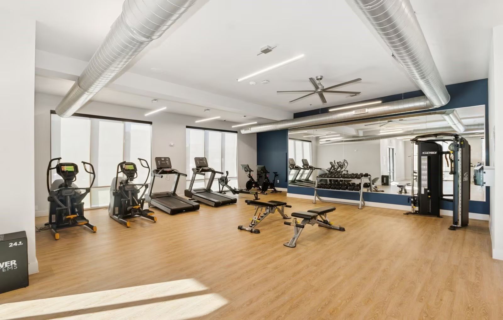 Bright modern gym with treadmills, weights, mirrors, and wood flooring