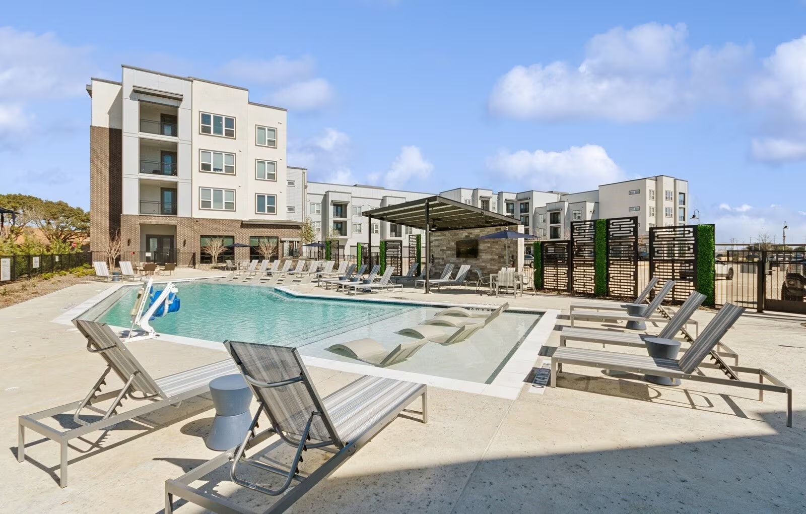 Modern resort pool area with lounge chairs, umbrellas, and a hotel building under a blue sky