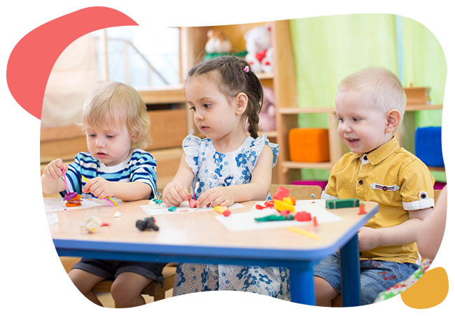 A group of children are sitting at a table playing with clay.