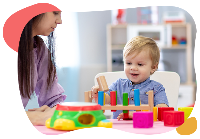 A woman is playing with a child who is sitting at a table with toys.