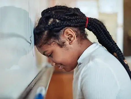 A young girl is leaning her head against a whiteboard.