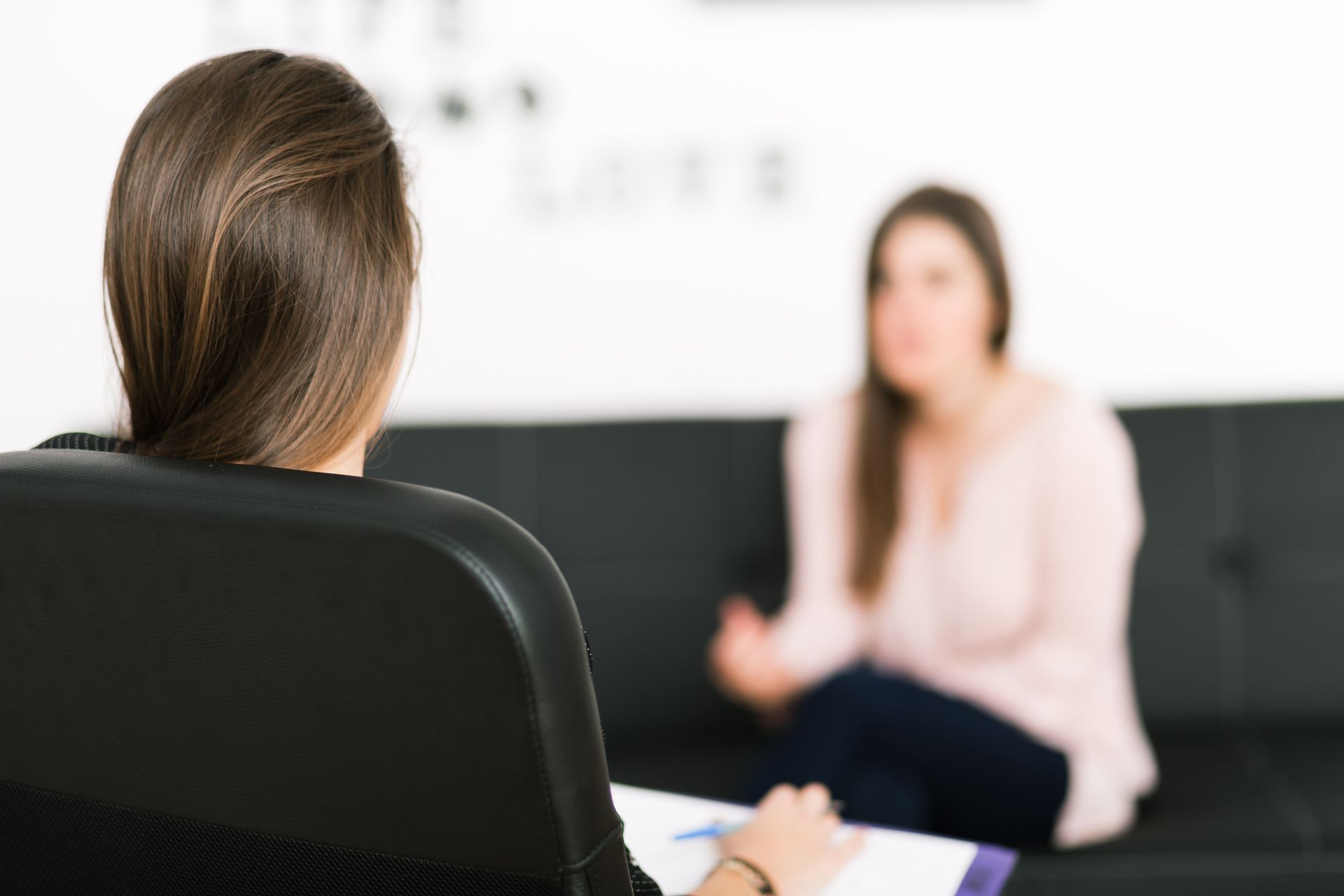 A woman is sitting on a couch talking to another woman.