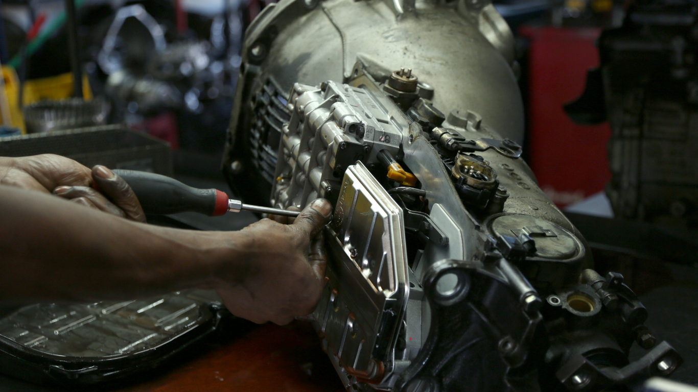 Hands working on a large metallic mechanical device on a workbench in a dim workshop