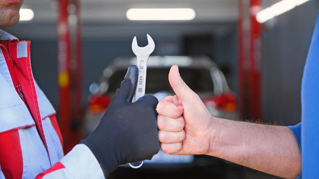 Mechanic in red uniform giving a thumbs-up beside a wrench in an auto shop