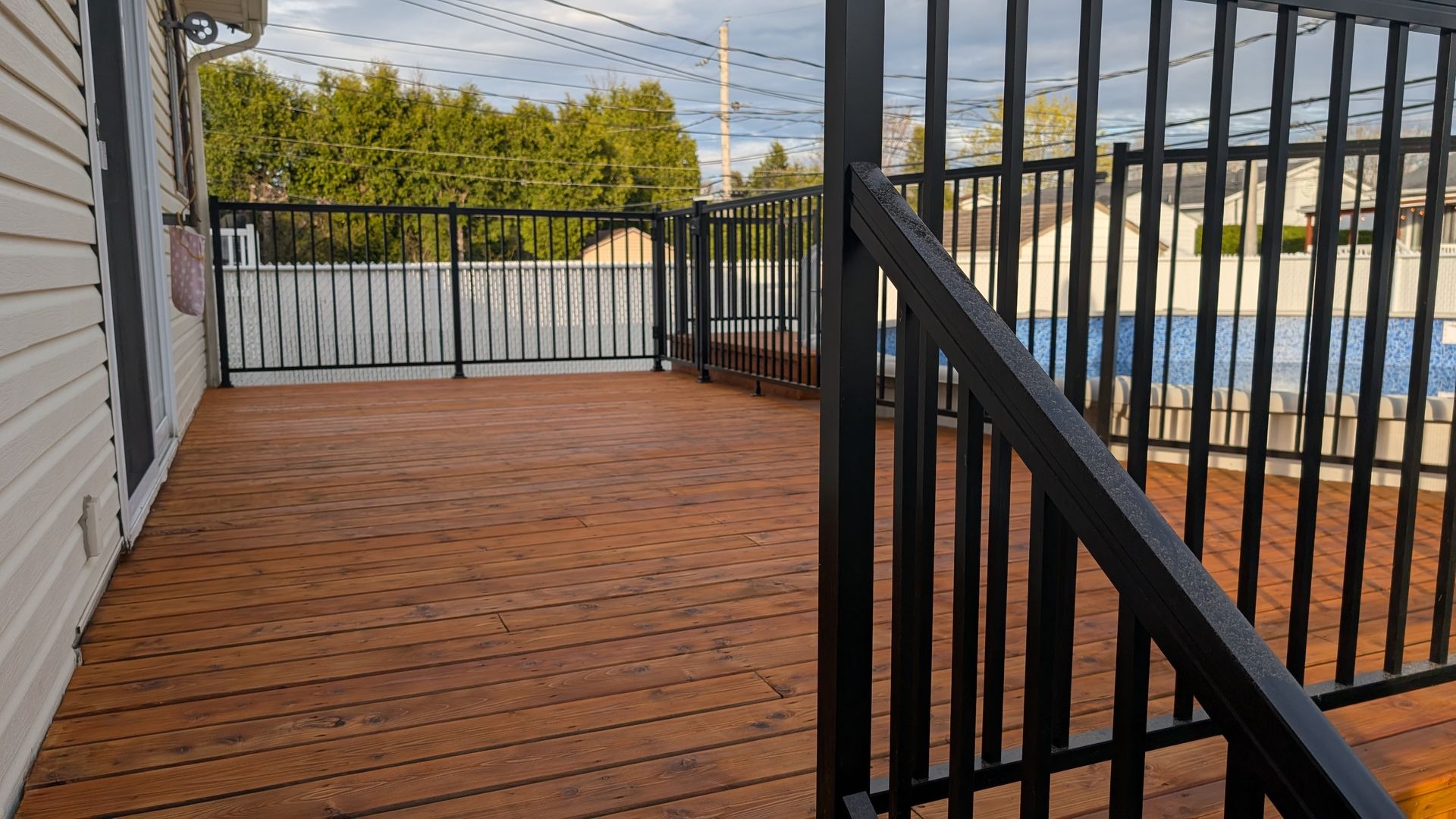 Terrasse en bois avec rambarde en métal noir donnant sur une piscine.