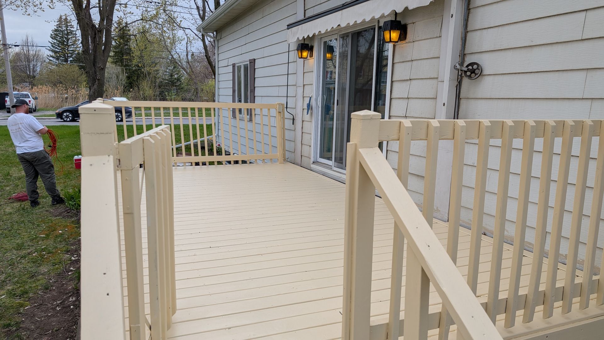 Terrasse en bois peinte en beige, avec une personne en arrière-plan, une maison et un jardin gazonné.