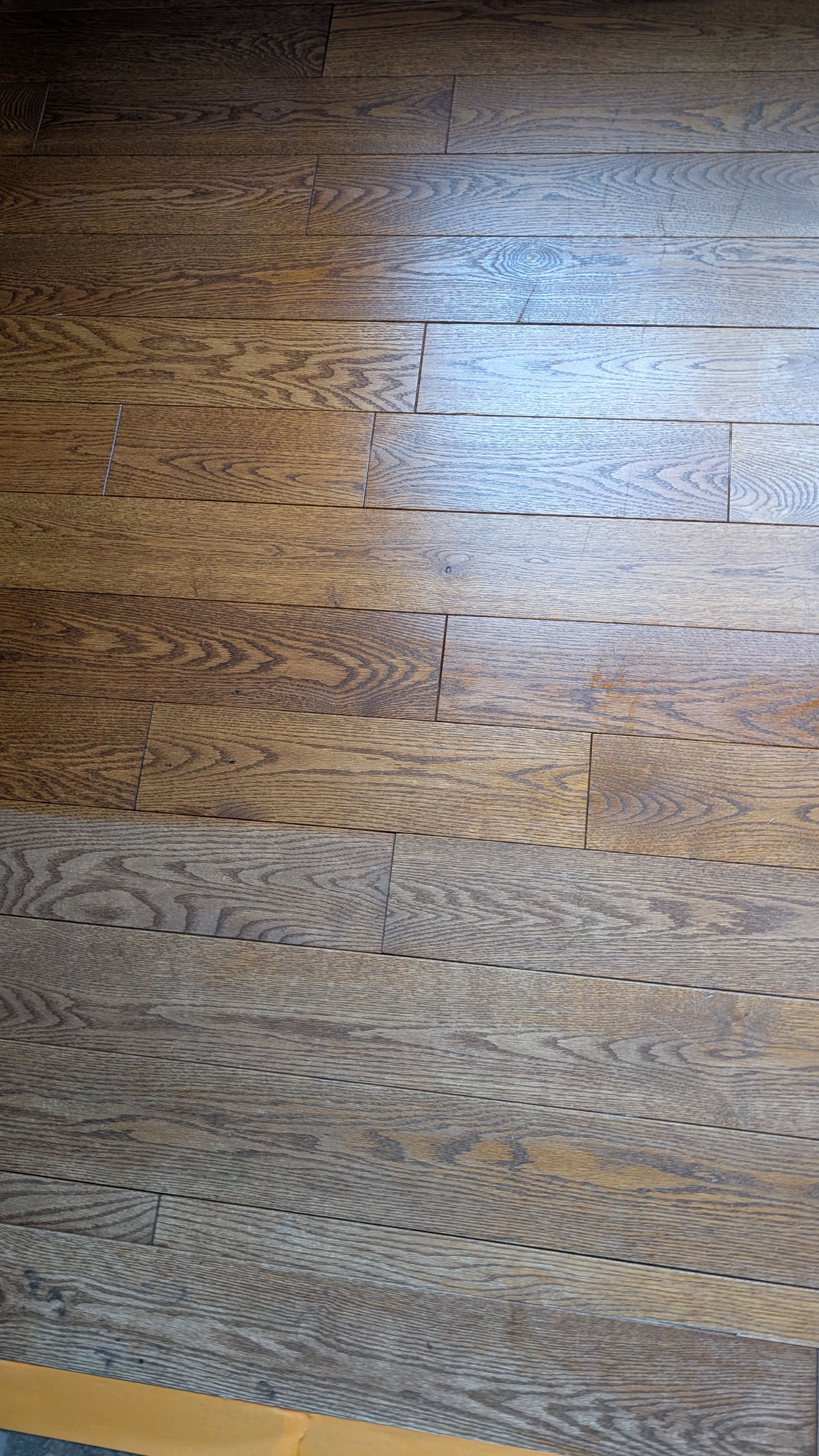 Plancher en bois, lames brun clair et brun foncé, quelques interstices visibles.