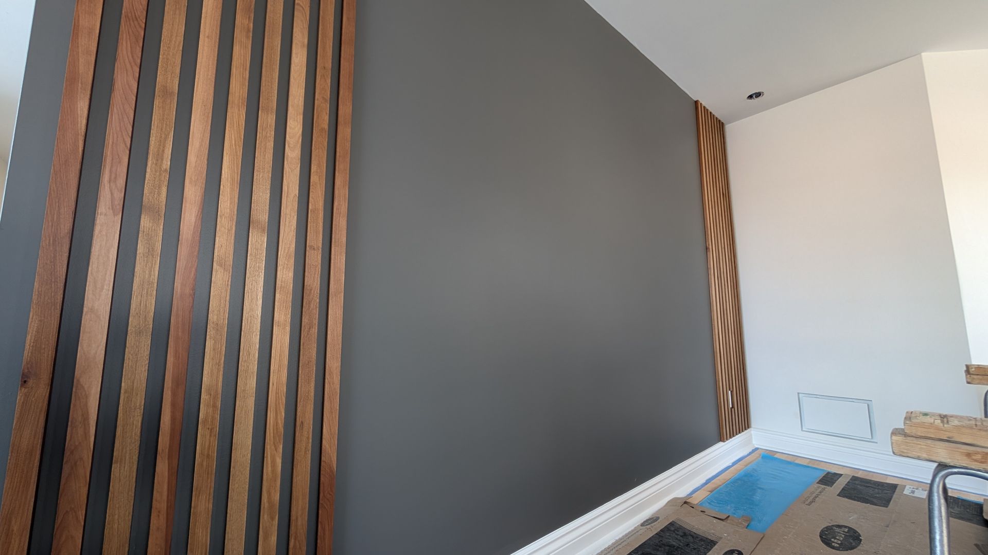 Mur en lattes de bois, murs peints en gris et blanc, et piscine bleue en arrière-plan.