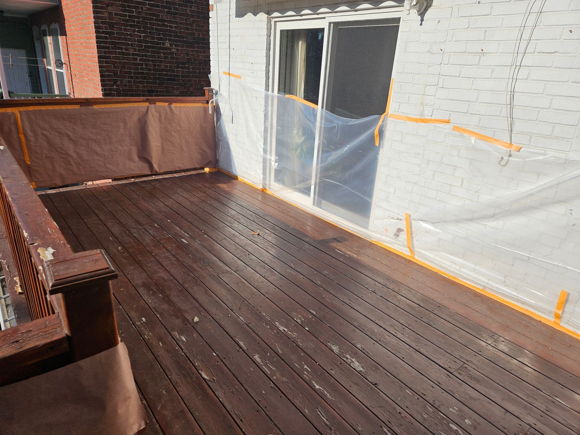 Terrasse en bois avec rambarde, adjacente à un mur recouvert d'une bâche en plastique.