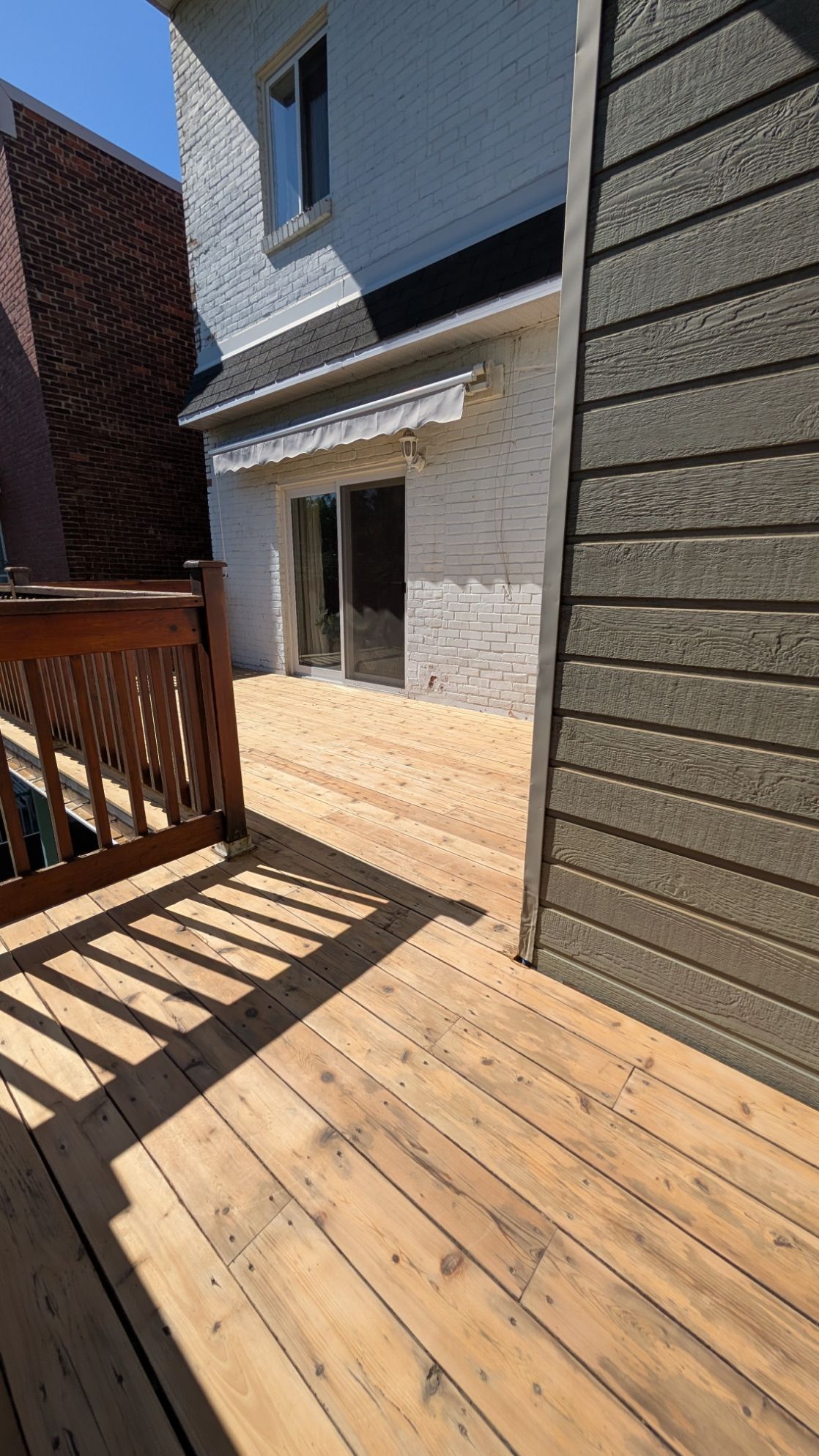 Terrasse en bois jouxtant un bâtiment à la façade en briques blanches et aux portes coulissantes en verre.