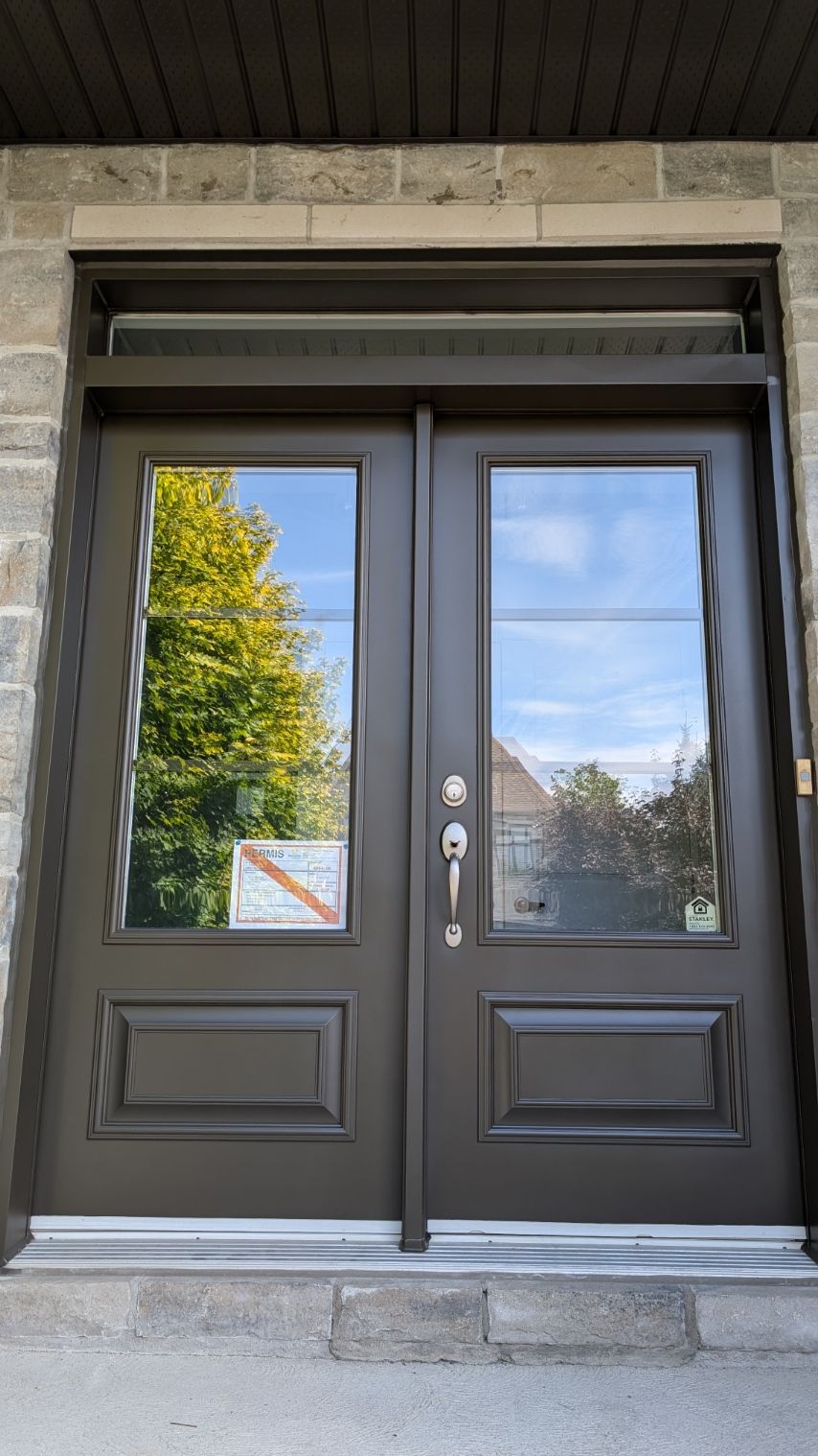 Double porte d'entrée marron avec grandes vitres et imposte ; façade en pierre.