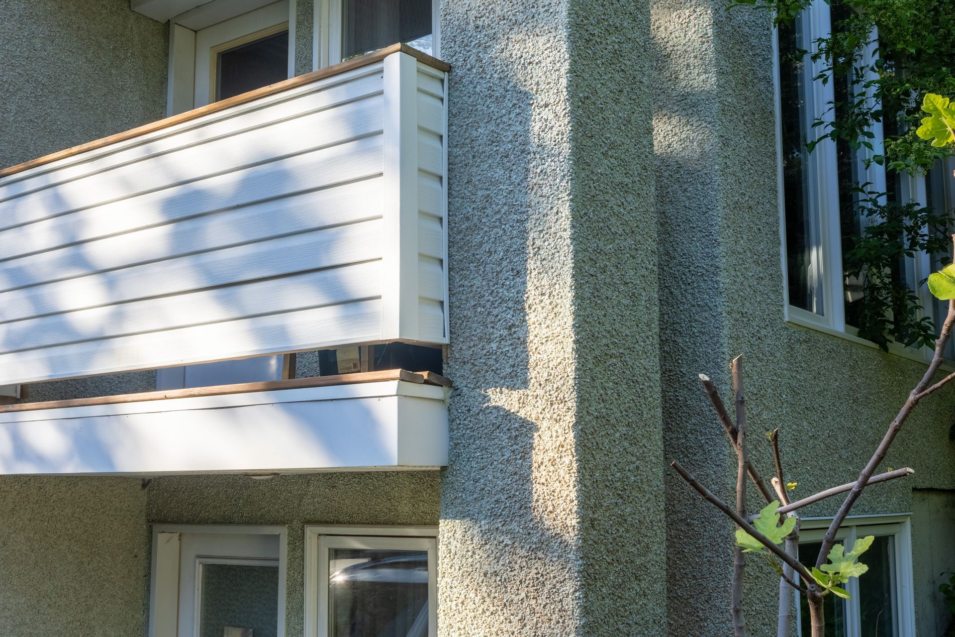 Balcon blanc sur un immeuble d'appartements en stuc présentant des dommages visibles et des boiseries apparentes