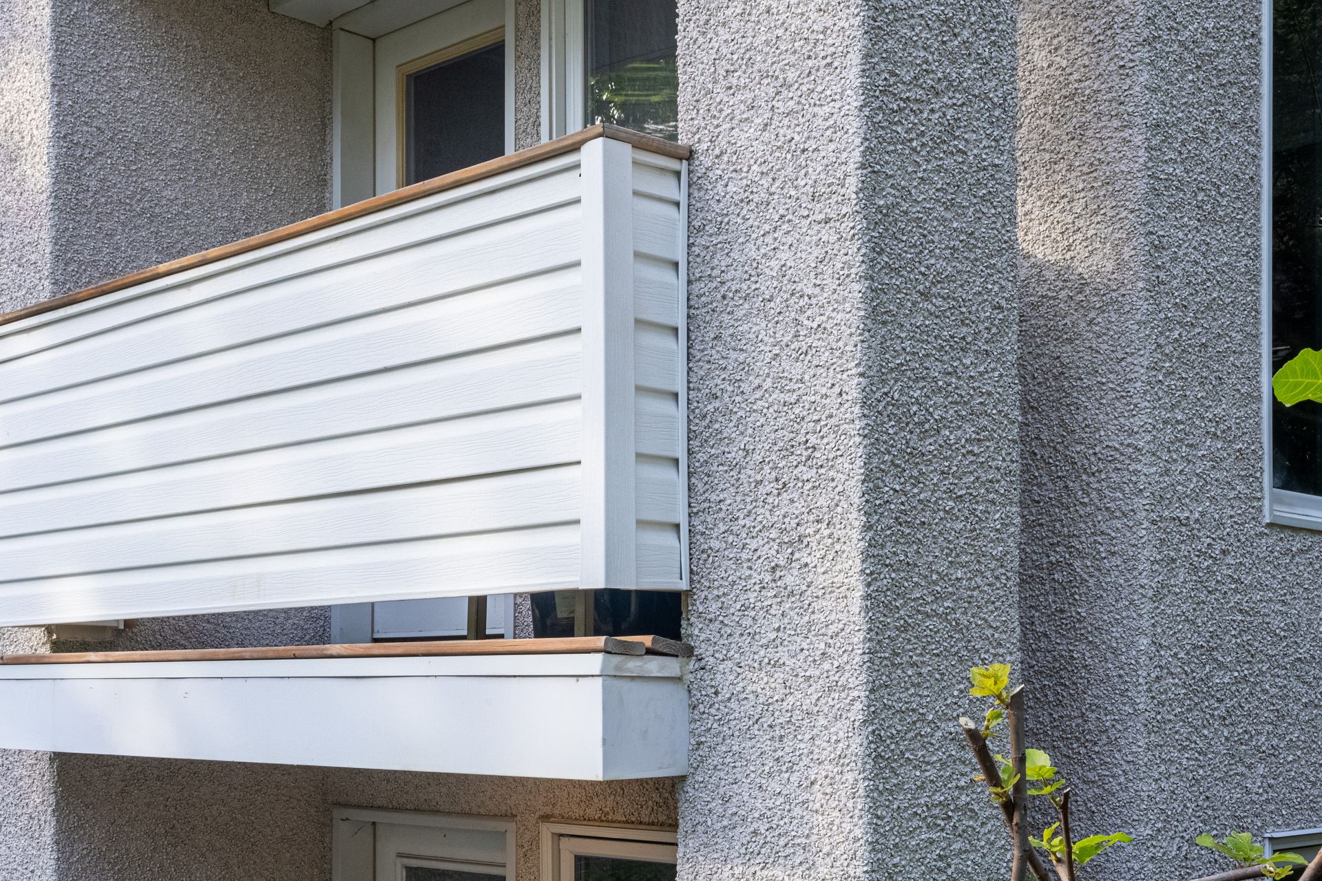 Balcon blanc avec bardage à lattes horizontales sur un bâtiment gris texturé.