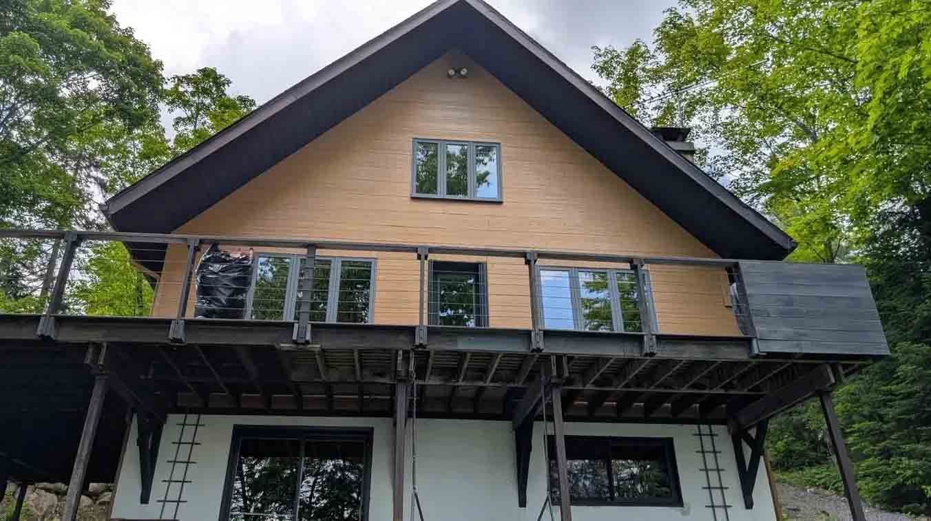 Maison à deux étages avec bardage en bois et finitions noires, grande terrasse, entourée d'arbres.