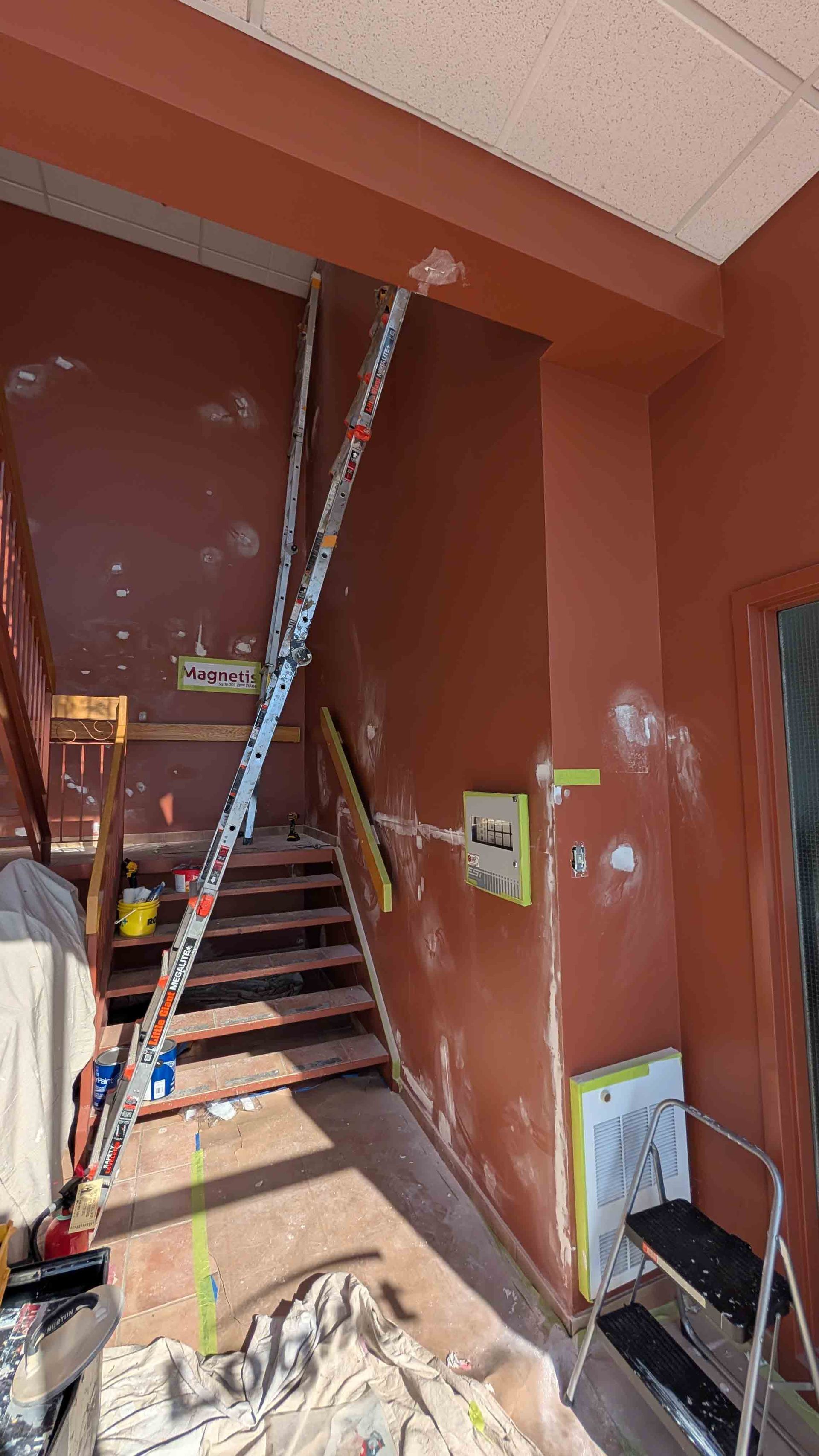 Cage d'escalier en construction avec échelles, outils et murs bruns dans un espace intérieur étroit