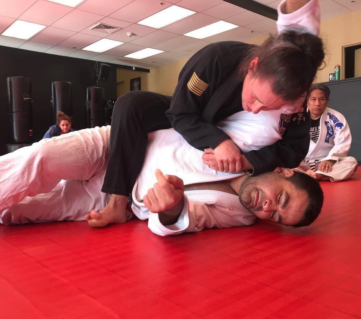 A man and a woman are wrestling on a red mat in a gym.