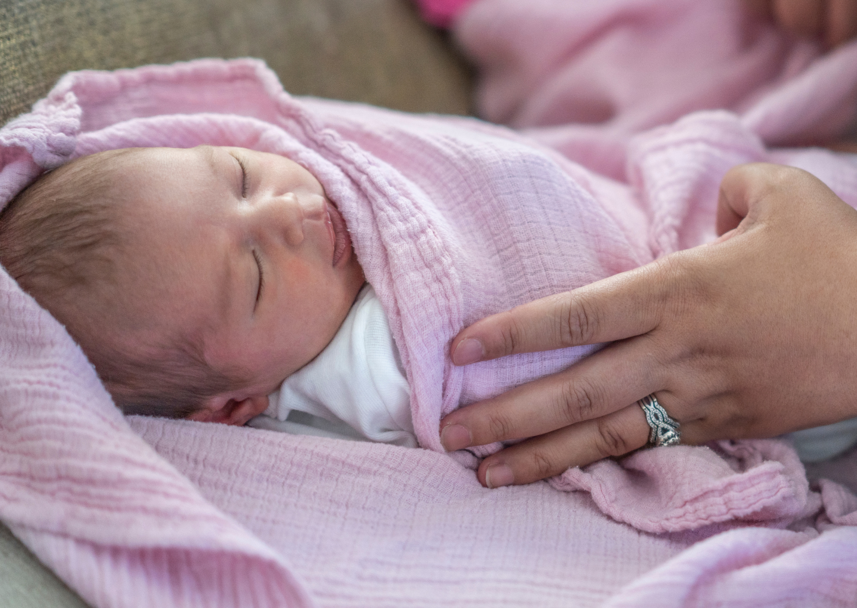 Uma mulher segura um bebê recém-nascido enrolado em um cobertor rosa.