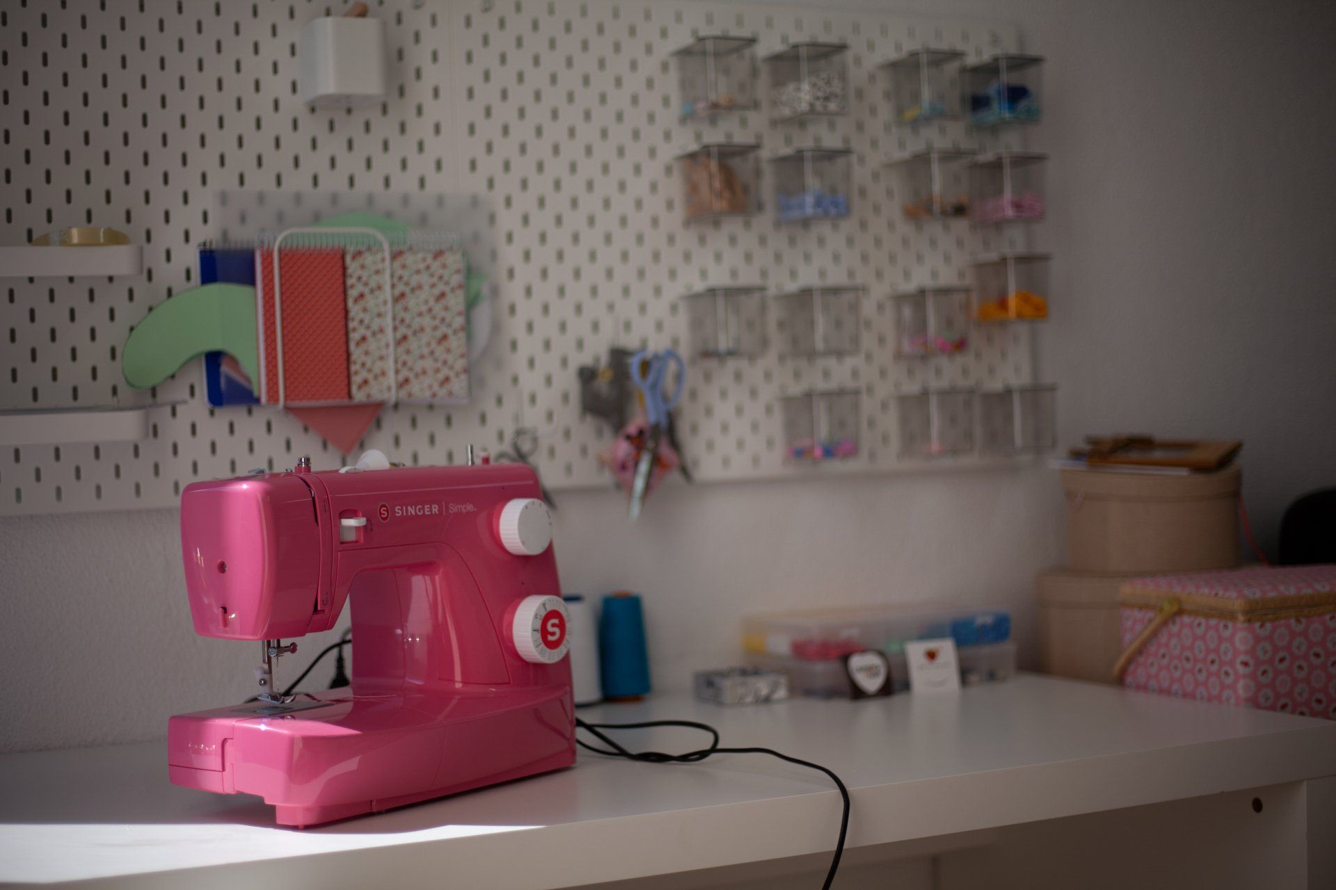 Uma máquina de costura rosa está sobre uma mesa branca em uma sala de artesanato.