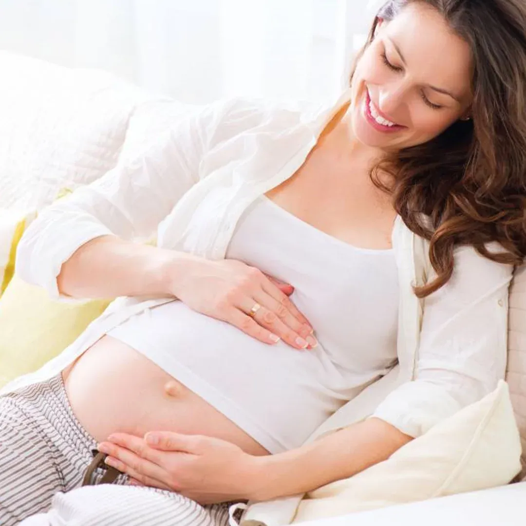 Uma mulher grávida está deitada no sofá com as mãos na barriga