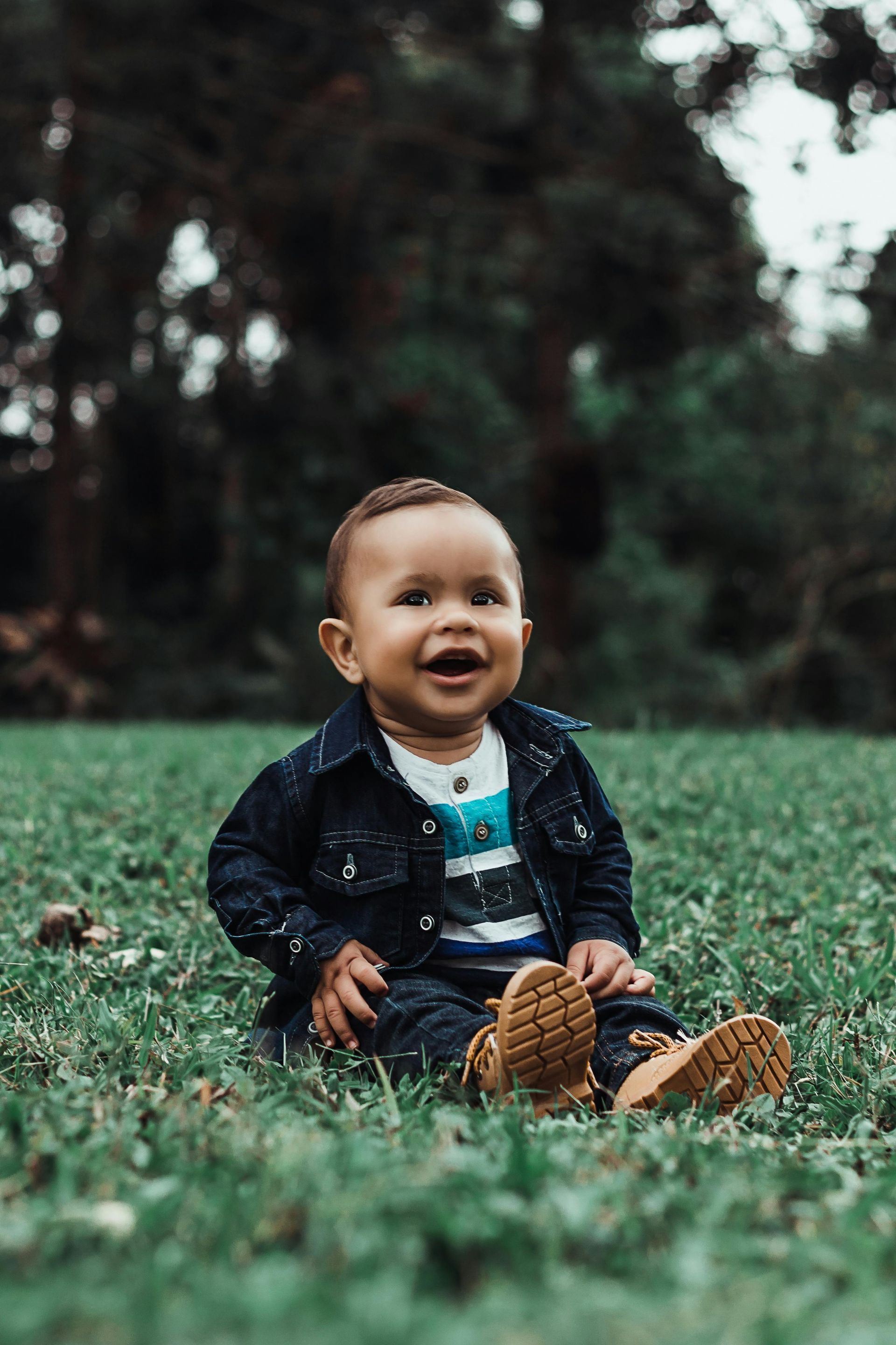 Um bebê está sentado na grama e sorrindo.