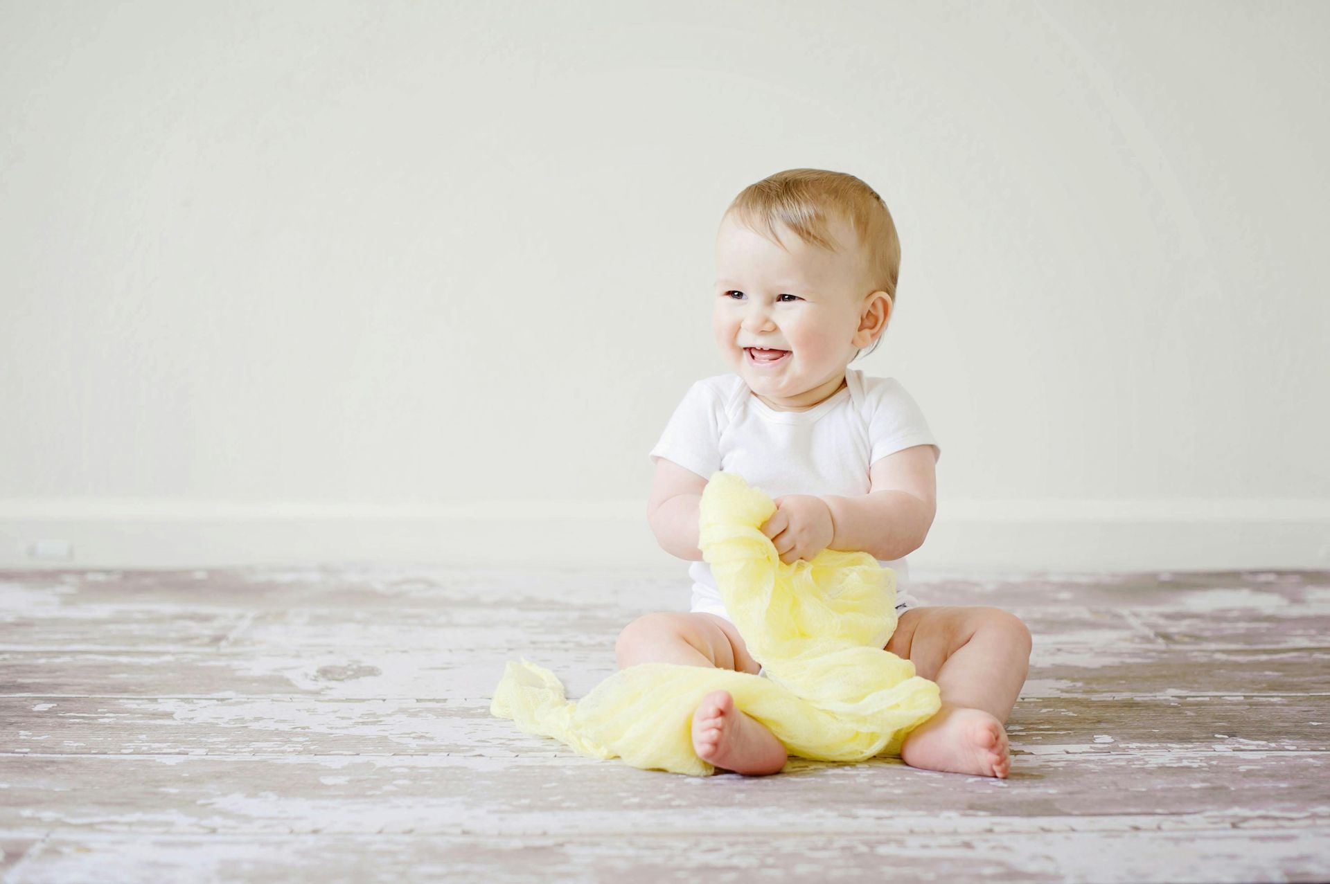 Um bebê está sentado no chão segurando um cobertor amarelo.
